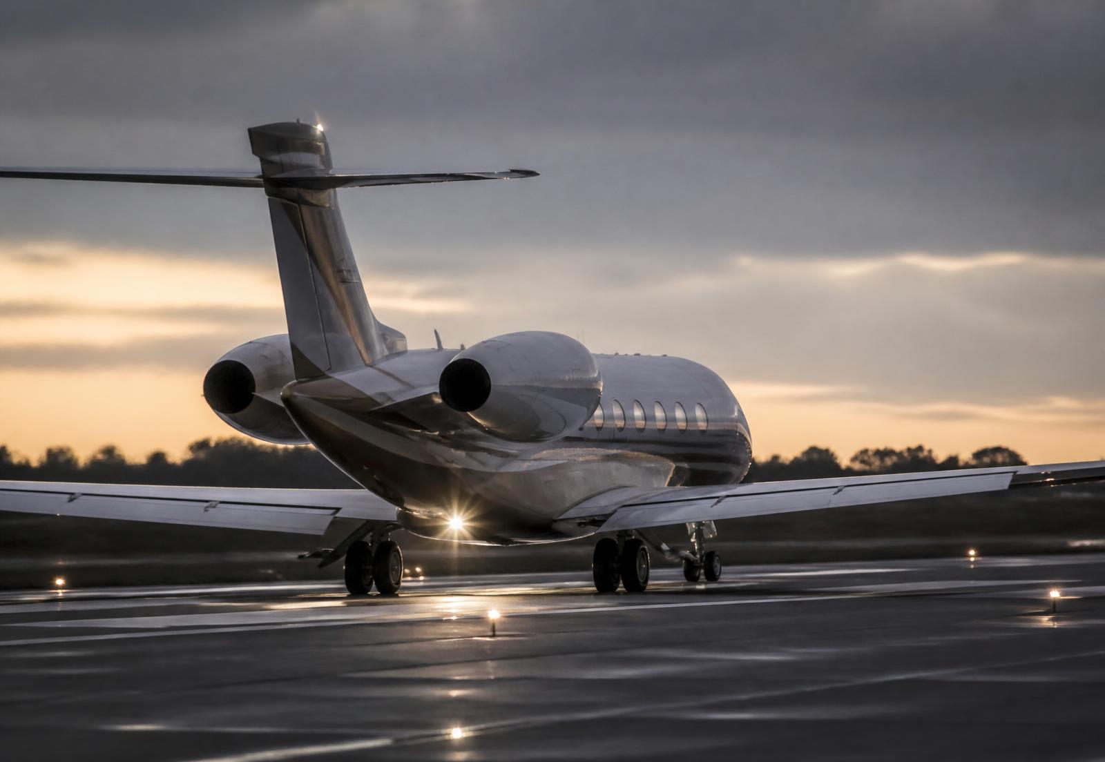 Business jet departing at dusk with runway lights reflecting on wet pavement