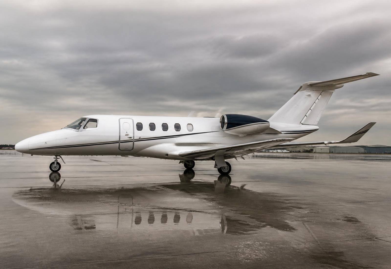 Light business jet in side profile on a wet ramp under overcast skies